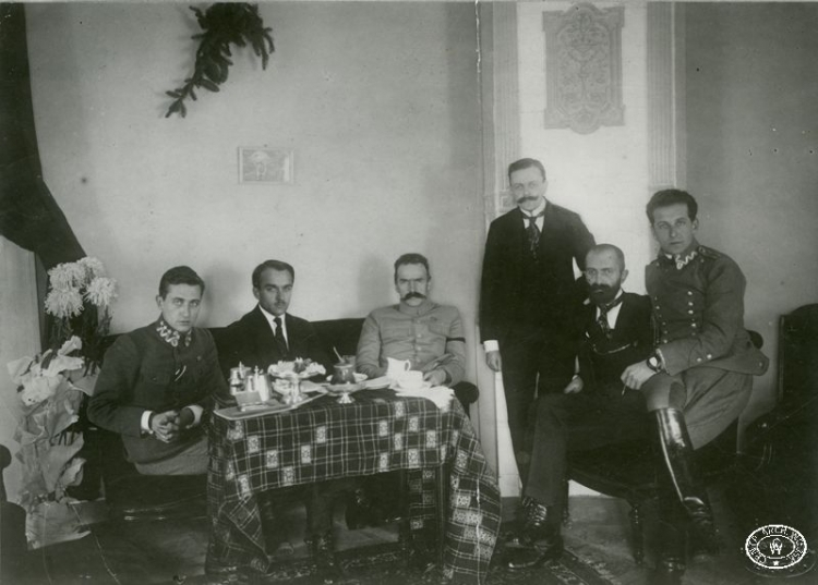 Komendant Józef Piłsudski w towarzystwie najbliższych współpracowników. Od lewej: Julian Stachiewicz, Tadeusz Kasprzycki, Józef Piłsudski, Michał Sokolnicki, Walery Sławek, Bolesław Długoszowski ps. „Wieniawa”. Hotel Brühla, Warszawa. 1917 r. Źródło: CAW