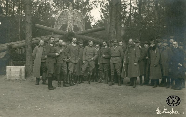 Oficerowie legionowi przed ziemianką komendy 4 Pułku Piechoty Legionów. Od lewej: kpt. Ferdynand Zarzycki, ppłk Henryk Minkiewicz, NN, ppłk Edward Rydz ps. „Śmigły”, płk Bolesław Roja, NN, płk Marian Januszajtis ps. „Żegota”, por. dr Leon Sternberg, mjr Michał Żymierski, NN, mjr Leon Berbecki, NN, mjr Andrzej Galica, kpt. Władysław Uzdowski ps. „Bończa”. 1. z prawej kpt. ks. kapelan Kazimierz Konopka, 5. (płaszcz z ciemnym kołnierzem)por. Mieczysław Więckowski. Rojowe Osiedle. Wołyń. Marzec 1916 r. CAW