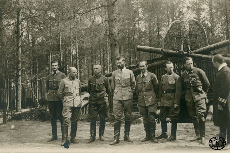 Oficerowie sztabu 4. Pułku Piechoty Legionów Polskich stoją przed kwaterą komendy pułku. Od lewej: chor. Henryk Doskocil, por. Jan Słuszkiewicz, kpt. Ferdynand Zarzycki, płk Bolesław Roja, kpt. dr Emil Bobrowski, chor. Józef Kempf-Gewont, chor. Józef Andrzej Teslar, kpt. ks. kapelan Kazimierz Konopka. Rojowe Osiedle, pozycje nad Styrem, Wołyń. Wiosna, 1916 r. Źródło: CAW