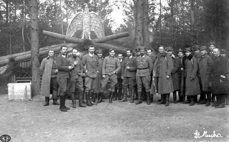 Oficerowie legionowi przed ziemianką komendy 4 Pułku Piechoty Legionów. Od lewej: kpt. Ferdynand Zarzycki, ppłk Henryk Minkiewicz, N.N., ppłk Edward Rydz ps. „Śmigły”, płk Bolesław Roja, N.N., płk Marian Januszajtis ps. „Żegota”, por. dr Leon Sternberg, mjr Michał Żymierski, N.N., mjr Leon Berbecki, N.N., mjr Andrzej Galica, kpt. Władysław Uzdowski ps. „Bończa”. Pierwszy z prawej kpt. ks. kapelan Kazimierz Konopka, piąty (w płaszczu z ciemnym kołnierzem) por. Mieczysław Więckowski. Rojowe Osiedle.  Fot. CAW