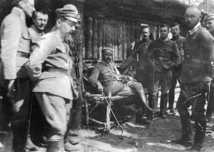 Brygadier Józef Piłsudski (siedzi w środku) w towarzystwie oficerów I Brygady Legionów Polskich. Widoczni m.in.: pułkownik Edward Rydz-Śmigły (z prawej na pierwszym planie), porucznik Bolesław Wieniawa-Długoszowski (za E. Rydzem-Śmigłym), major Michał Żymierski (stoi 2. z lewej na drugim planie, z rękami w kieszeniach), wiosna 1916. Źródło: NAC