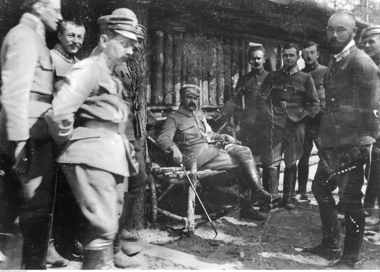 Wołyń, 1916 r. Oficerowie I Brygady Legionów Polskich: brygadier Józef Piłsudski (siedzi w środku) w towarzystwie oficerów I Brygady Legionów Polskich. Widoczni m.in.: płk Edward Rydz-Śmigły (z prawej na pierwszym planie), por. Bolesław Wieniawa-Długoszowski (za E. Rydzem-Śmigłym), mjr Michał Żymierski (stoi 2. z lewej na drugim planie, z rękami w kieszeniach). Źródło: NAC Wołyń, 1916 r. Oficerowie I Brygady Legionów Polskich: brygadier Józef Piłsudski (siedzi w środku) w towarzystwie oficerów I Brygady Legionów Polskich. Widoczni m.in.: płk Edward Rydz-Śmigły (z prawej na pierwszym planie), por. Bolesław Wieniawa-Długoszowski (za E. Rydzem-Śmigłym), mjr Michał Żymierski (stoi 2. z lewej na drugim planie, z rękami w kieszeniach). Źródło: NAC