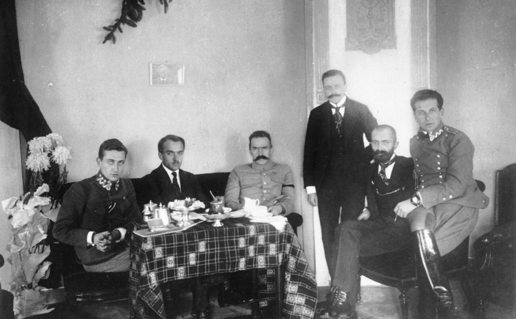 Grudzień 1916 r. Śniadanie u Józefa Piłsudskiego w hotelu w Warszawie. Siedzą od lewej: Julian Stachiewicz, Tadeusz Kasprzycki, Józef Piłsudski, Michał Sokolnicki (stoi), Walery Sławek, Bolesław Wieniawa-Długoszowski. Źródło: Narodowe Archiwum Cyfrowe