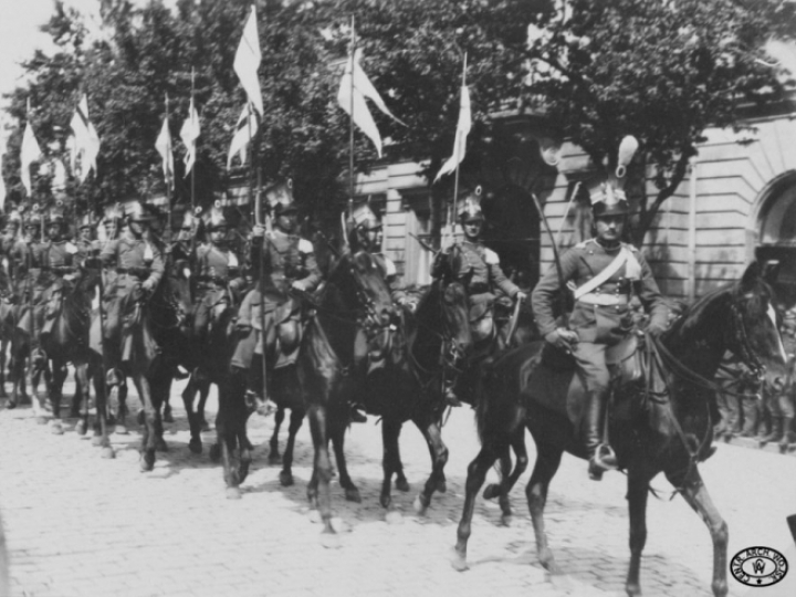 Szwadron 2. Pułku Ułanów Legionów Polskich wyjeżdża z Placu Saskiego. W tle widoczny budynek Hotelu Europejskiego, w głębi sobór św. Aleksandra Newskiego. Warszawa. Wiosna 1917 r. Źródło: CAW