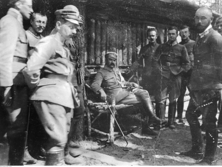 Wołyń, 1916 r. Oficerowie I Brygady Legionów Polskich: brygadier Józef Piłsudski (siedzi w środku) w towarzystwie oficerów I Brygady Legionów Polskich. Widoczni m.in.: płk Edward Rydz-Śmigły (z prawej na pierwszym planie), por. Bolesław Wieniawa-Długoszowski (za E. Rydzem-Śmigłym), mjr Michał Żymierski (stoi 2. z lewej na drugim planie, z rękami w kieszeniach). Źródło: NAC
